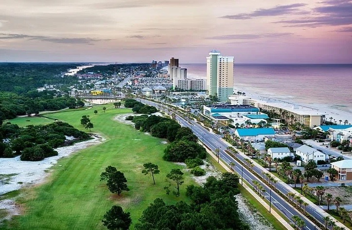 Panama City Beach at dusk: condo towers along the Gulf, the beachfront road, and a golf course in the foreground
